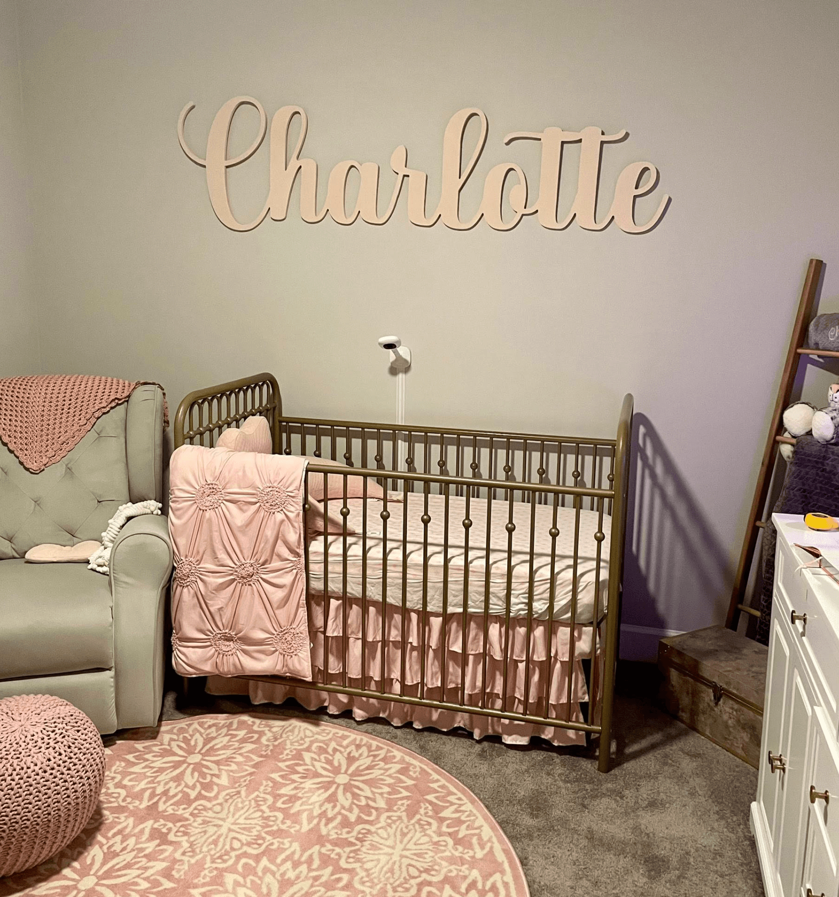 Custom cut wood script name sign mounted on a nursery wall above a brass crib