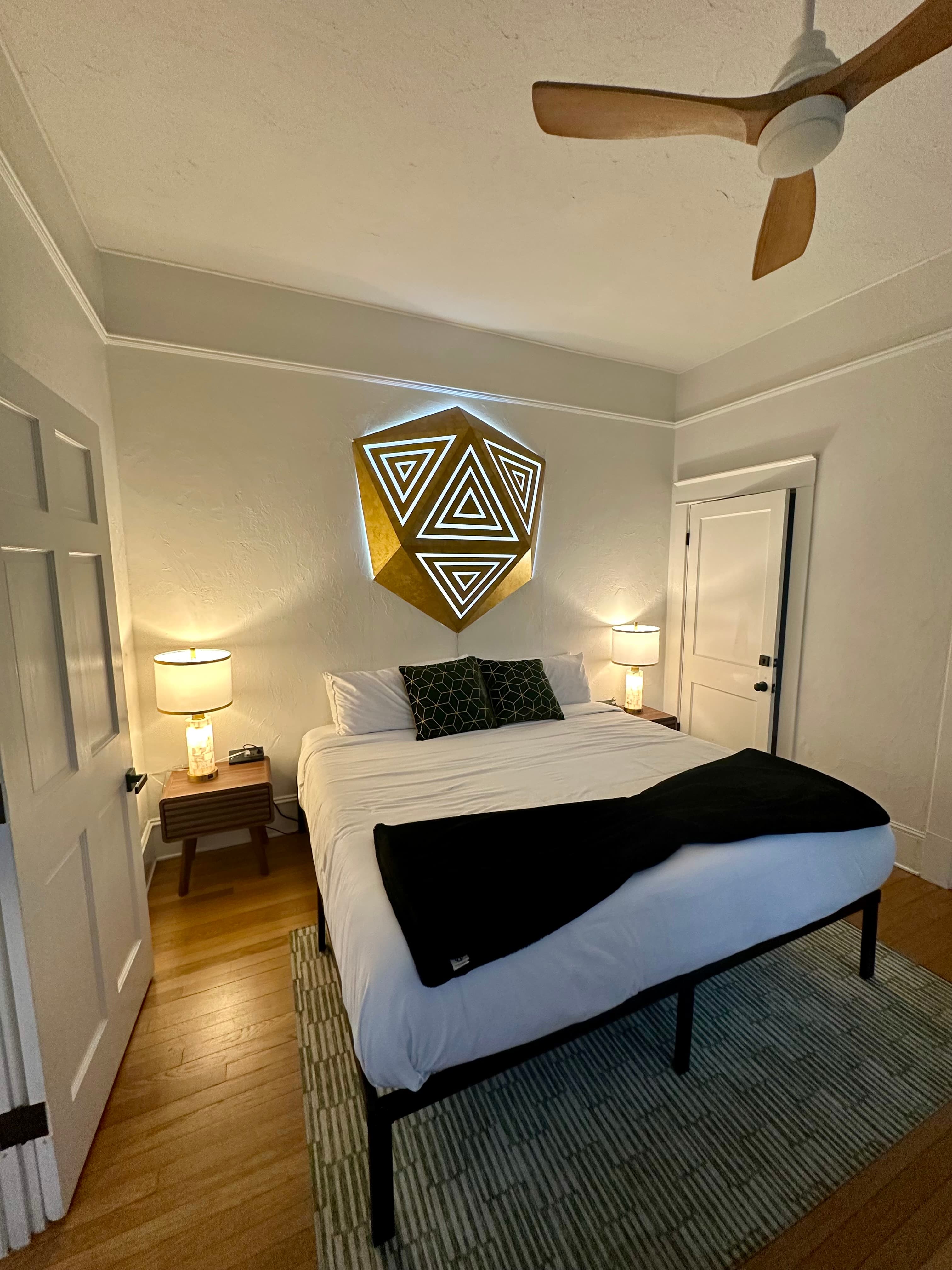 Gold faceted wall panel with glowing white triangle inlays and an LED halo in a dark bedroom