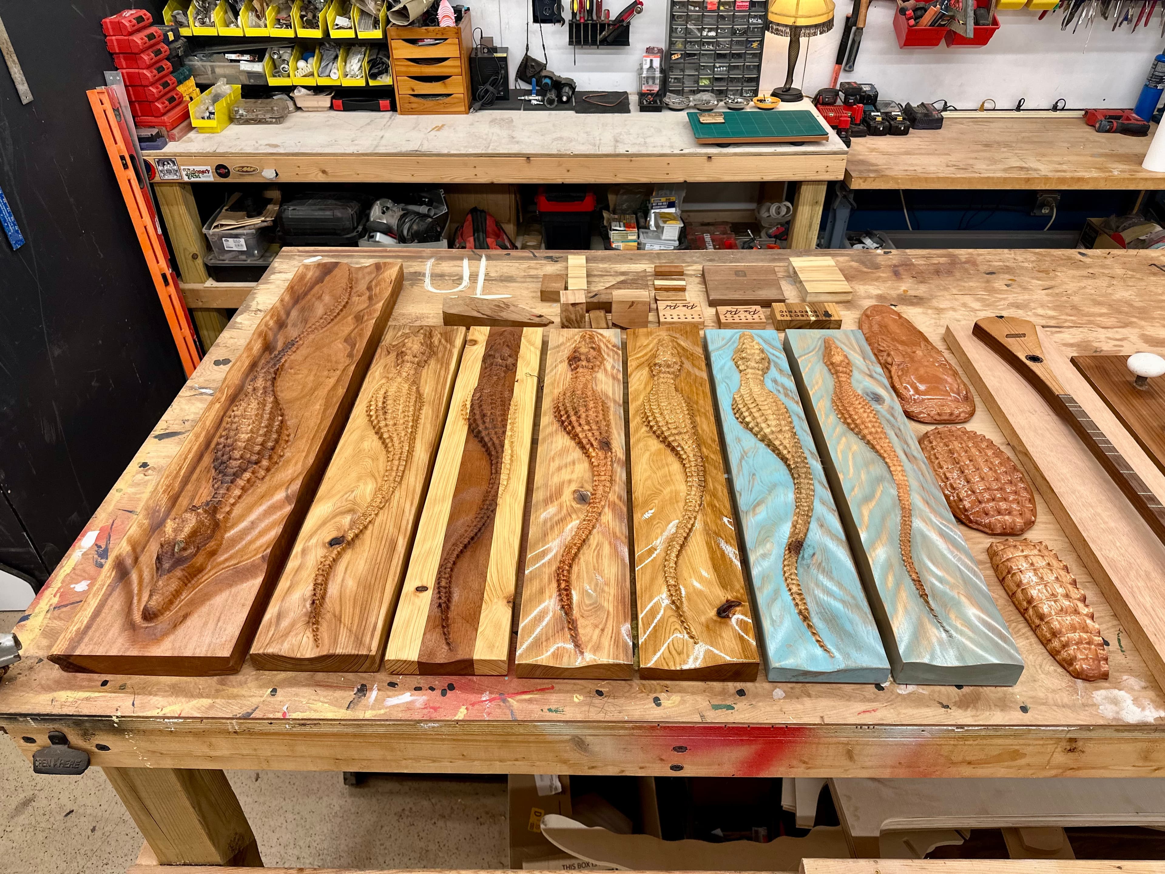 Bench-top lineup of carved alligator relief boards in walnut, blond ash and turquoise resin finishes