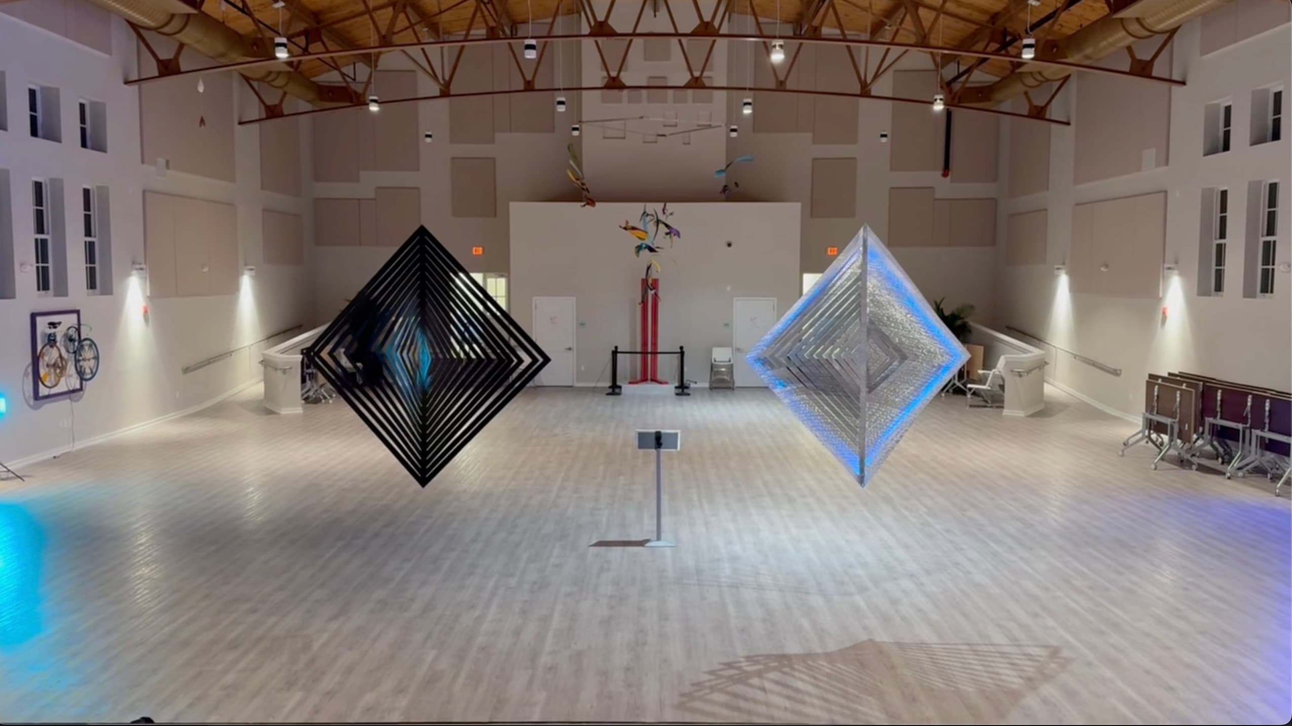 Two large diamond kinetic spinner sculptures, one matte black and one mirrored with blue LED glow, suspended in an event hall